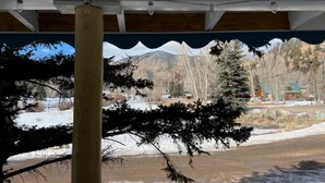 A view through a window with a wooden beam and a snow-covered landscape, including trees and a building in the background. - Room 10 at Bellamy's (Red River)
