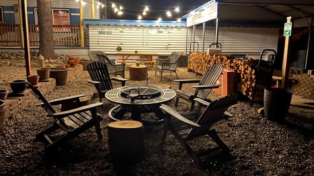 An outdoor seating area with a round table and chairs, surrounded by firewood and potted plants. - Room 10 at Bellamy's (Red River)