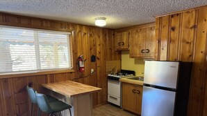 A compact kitchen with wooden cabinets, a gas stove, a refrigerator, and a bar stool. - Room 10 at Bellamy's (Red River)