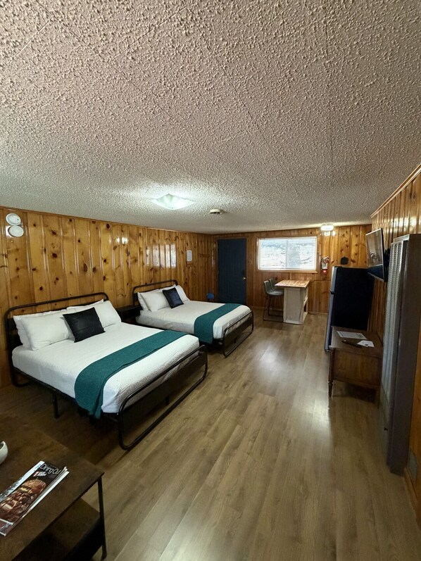 A room with two beds, a desk, a chair, a refrigerator, and a window. - Room 10 at Bellamy's (Red River)