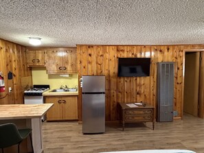 A kitchen with wooden cabinets, a refrigerator, a stove, a sink, a television, and a small table. - Room 10 at Bellamy's (Red River)
