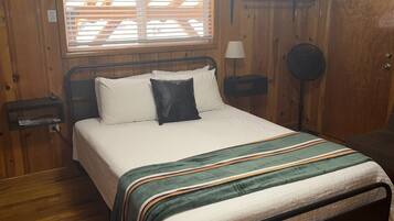 A wooden-paneled bedroom with a bed, a window with blinds, a bedside lamp, and a floor lamp.