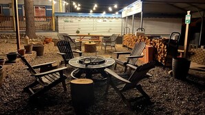 An outdoor seating area with a round table and chairs, surrounded by firewood and potted plants. - Room 5 at Bellamy's Haus (Red River)
