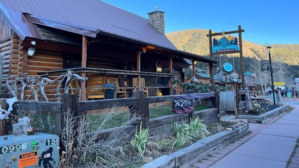 A rustic log cabin with a metal roof, a sign for 'Noble Wines Winery & Grape', and a wooden fence with a 'CAUTION HIGH VOLTAGE' sign. - Room 5 at Bellamy's Haus (Red River)