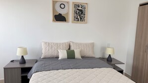 Une chambre à coucher comprenant un lit, deux tables de chevet, deux lampes fixées au mur, une armoire et deux œuvres d’art encadrées.