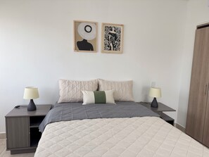 A bedroom with a bed, two bedside tables, two wall-mounted lamps, a wardrobe, and two framed artworks. - Serena Del Mar: Apartment Trevi 5 minutes from private beach. (Bolívar)