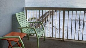 Varanda com vista para uma praia e um cais. Há duas cadeiras e uma mesa pequena.