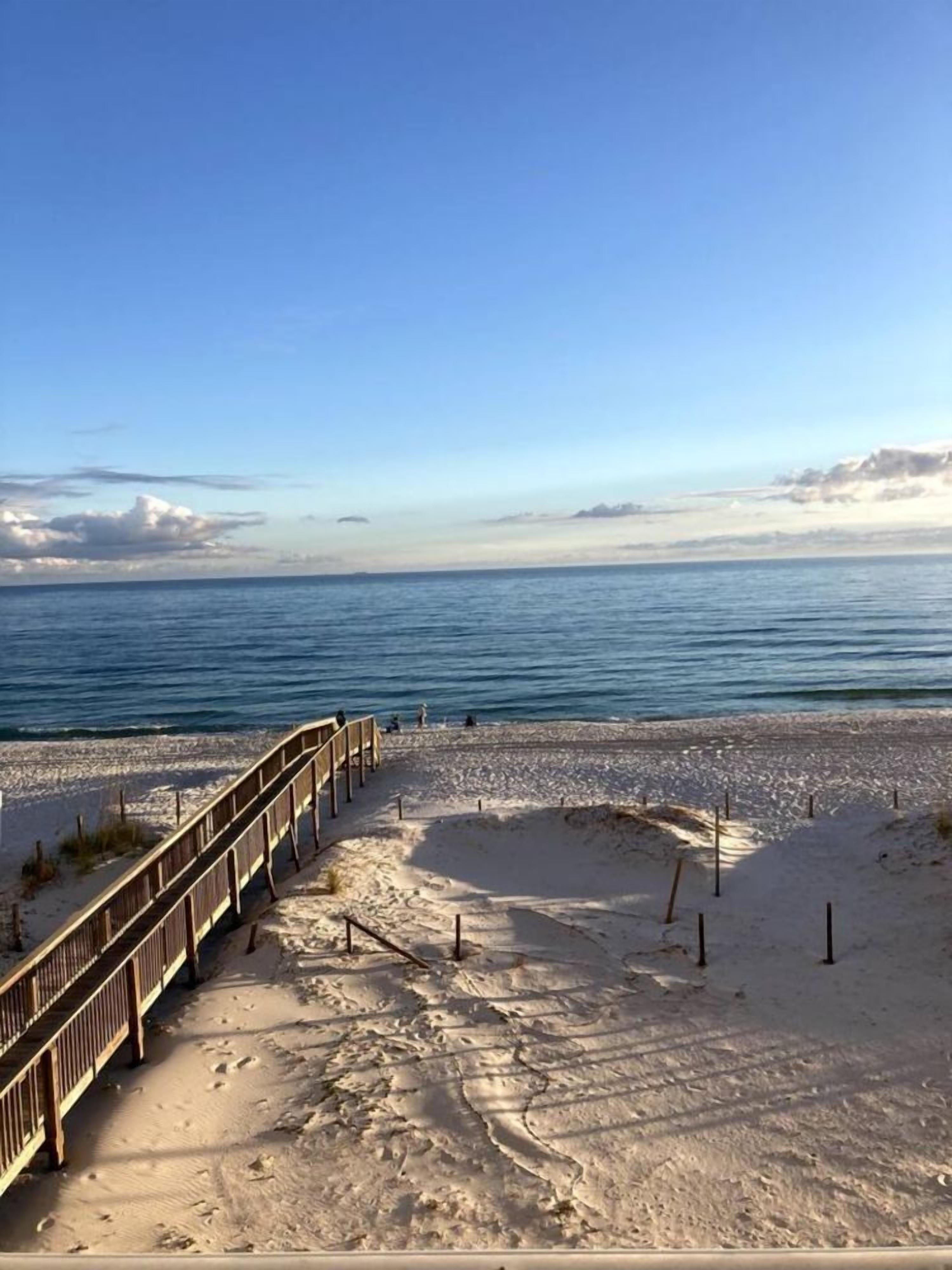 Ein Sandstrand mit einer Holzpromenade, die zum Wasser führt.