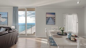Un salon moderne avec vue sur l’océan, un coin repas avec une table dressée pour deux personnes et un espace salon confortable avec un canapé.
