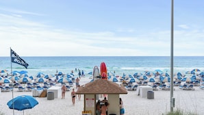 A beach with rows of sun umbrellas, a lifeguard tower, and a flag. - Tidewater Horizon by Avantstay Beachfront Condo + Indoor Pool + Spa Amenities + Movie Theater + Near Pier Park (Panama City Beach)