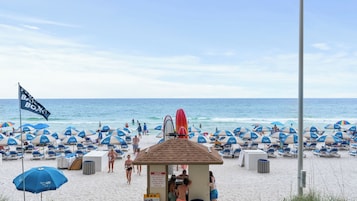 A beach with rows of sun umbrellas, a lifeguard tower, and a flag.