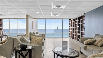 A spacious room with a large window overlooking the sea, a comfortable seating area, and a bookshelf.