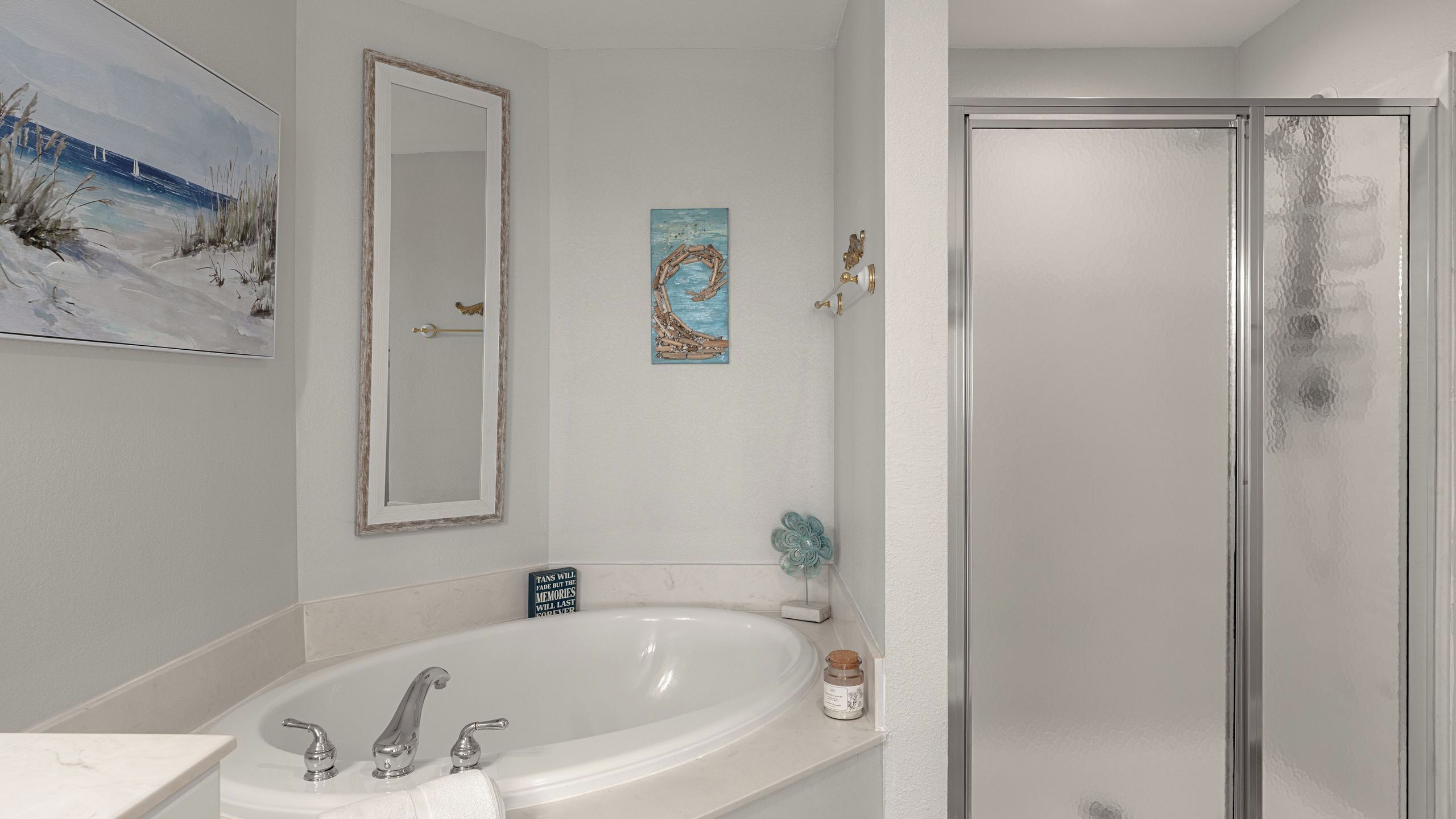 A bathroom with a bathtub, a glass shower enclosure, a mirror, and a painting on the wall.
