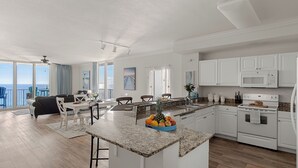 A modern kitchen with granite countertops, white cabinetry, and a central island with fruit. - Tidewater Horizon by Avantstay Beachfront Condo + Indoor Pool + Spa Amenities + Movie Theater + Near Pier Park (Panama City Beach)