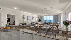A modern kitchen with granite countertops, a dishwasher, and a dining area with a view of the ocean. - Tidewater Horizon by Avantstay Beachfront Condo + Indoor Pool + Spa Amenities + Movie Theater + Near Pier Park (Panama City Beach)