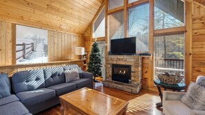A cozy cabin interior with a stone fireplace, a large window, and a television. - Grand Getaway Cabin by Avantstay A-frame Retreat + Hot Tub + Pool Access, Game Room Mins to Dollywood (Sevierville)