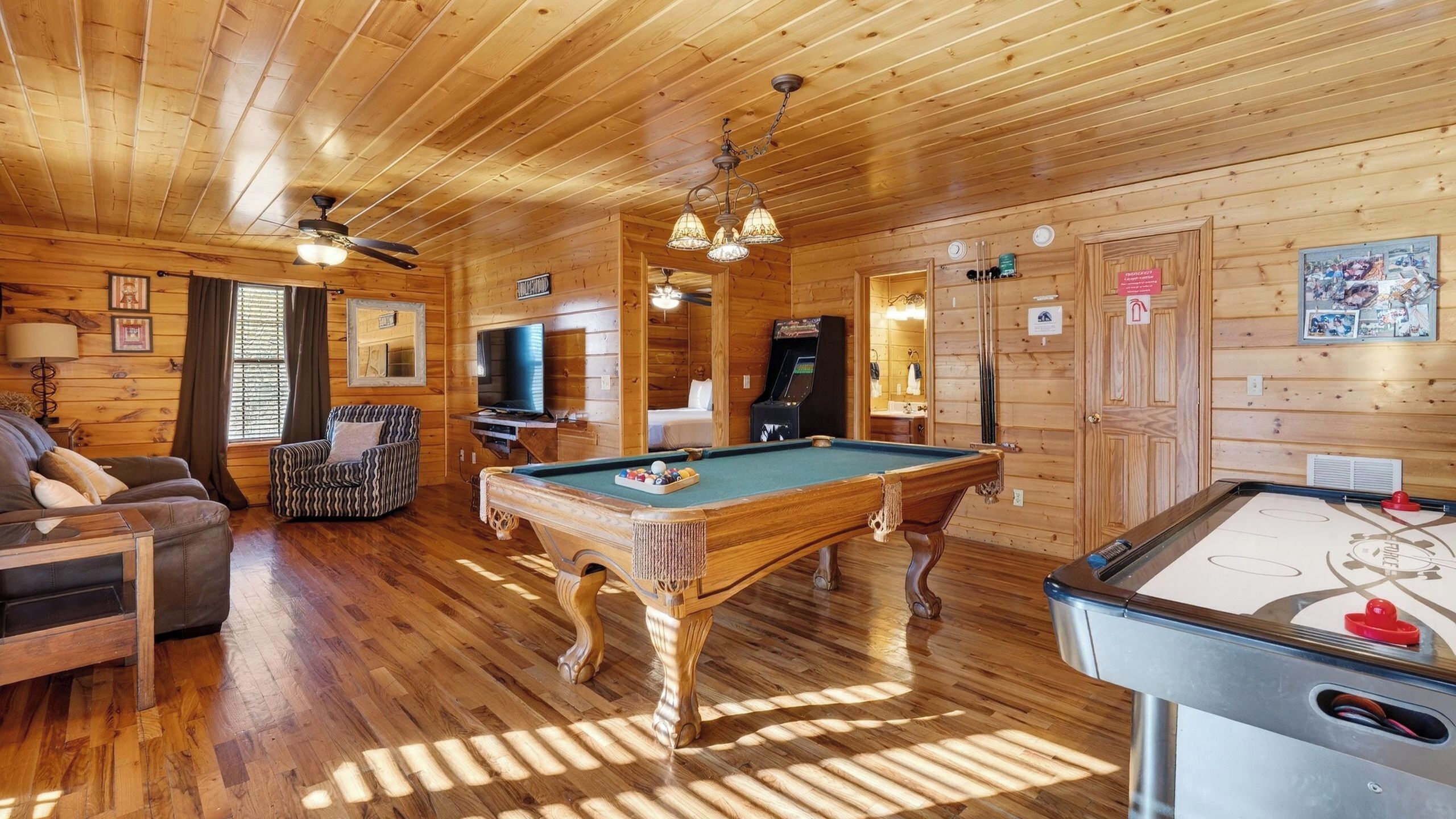 A wooden cabin interior with a pool table, a sofa, a television, and a ceiling fan.