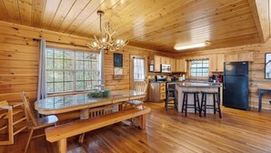 A wooden cabin interior with a dining area, kitchen, and bar seating. - Grand Getaway Cabin by Avantstay A-frame Retreat + Hot Tub + Pool Access, Game Room Mins to Dollywood (Sevierville)