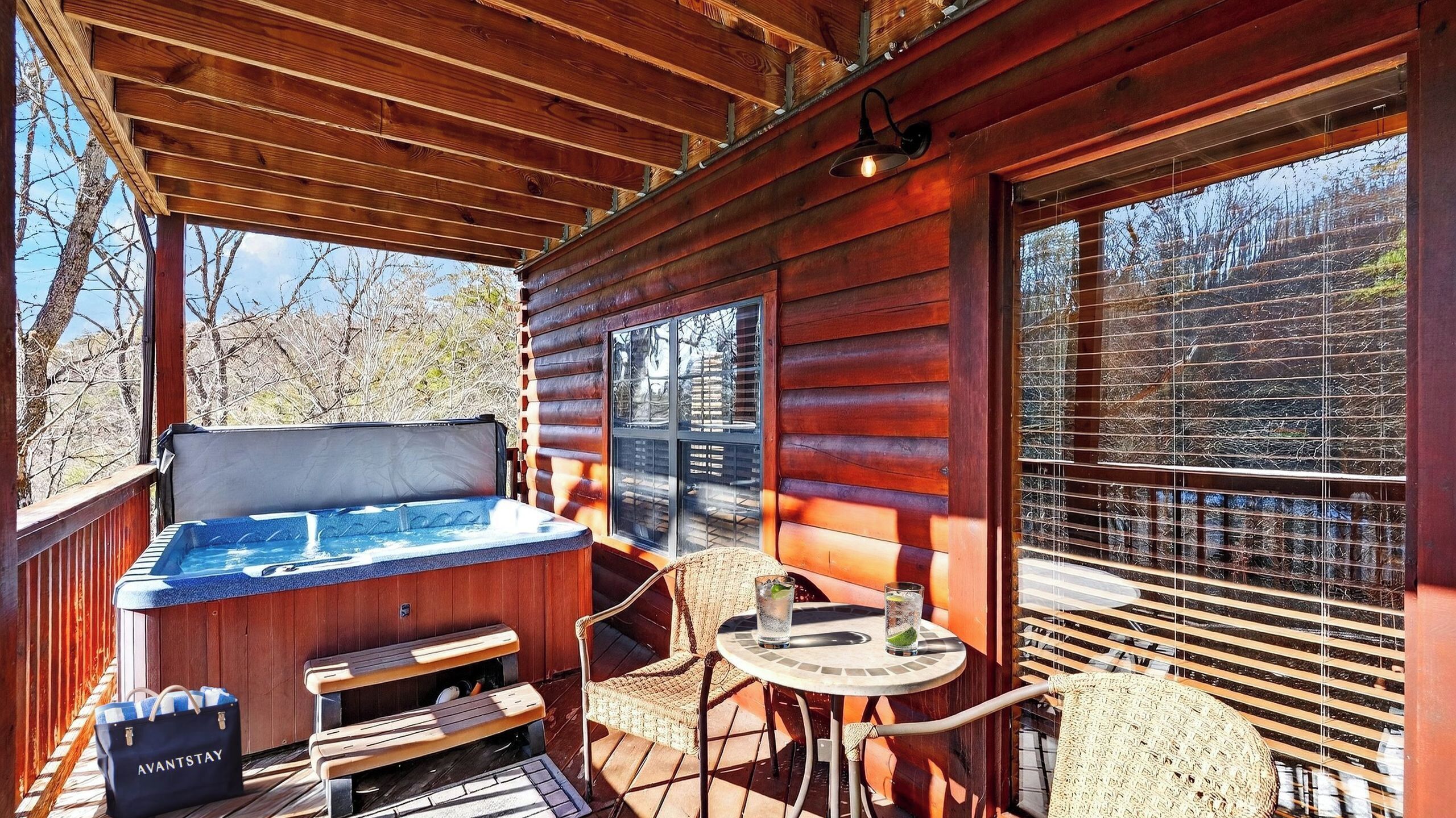 A wooden deck with a hot tub, a table, chairs, and a view of trees.