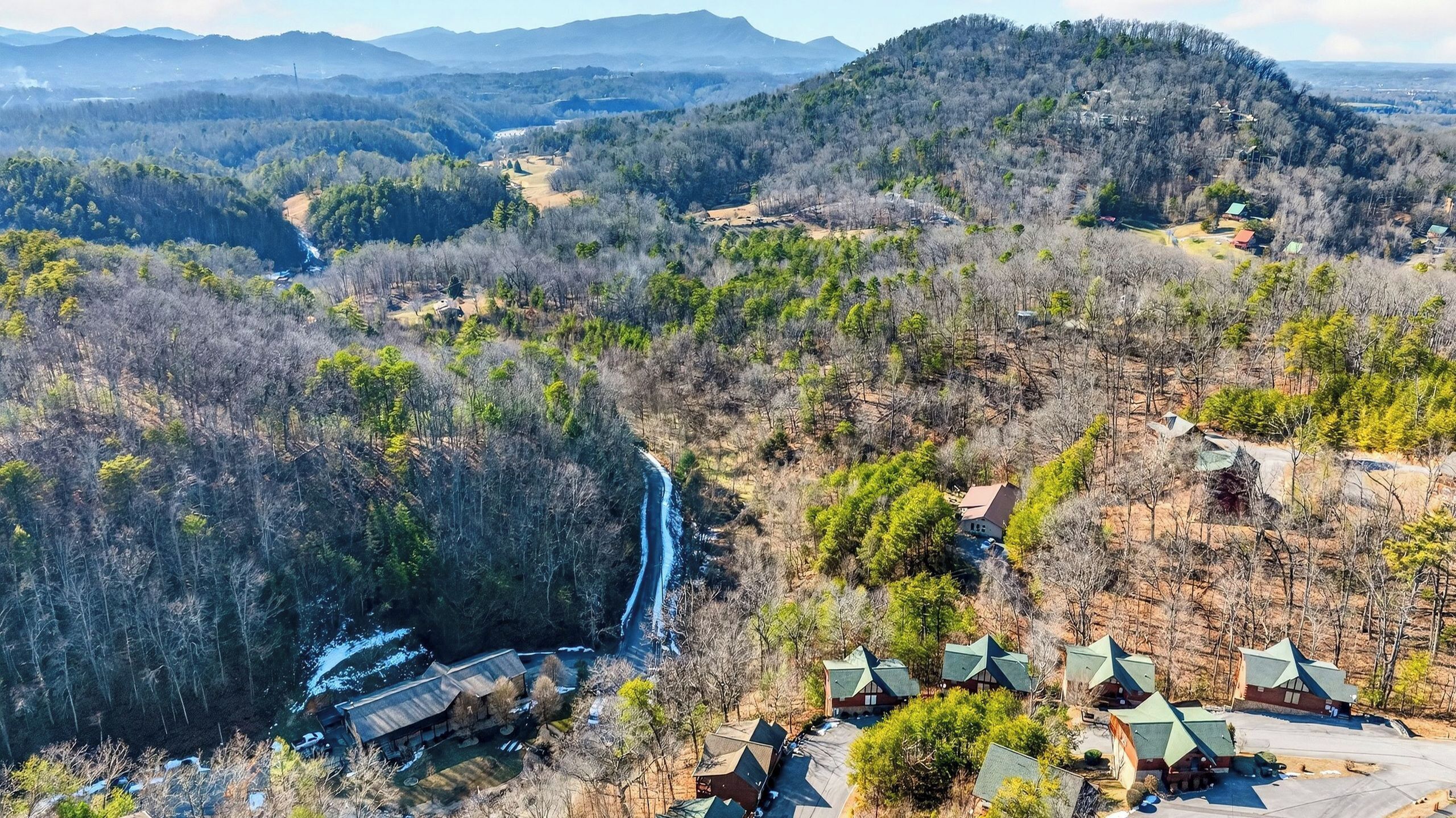 A mountainous area with a river, cabins, and a large building with a sloped roof.