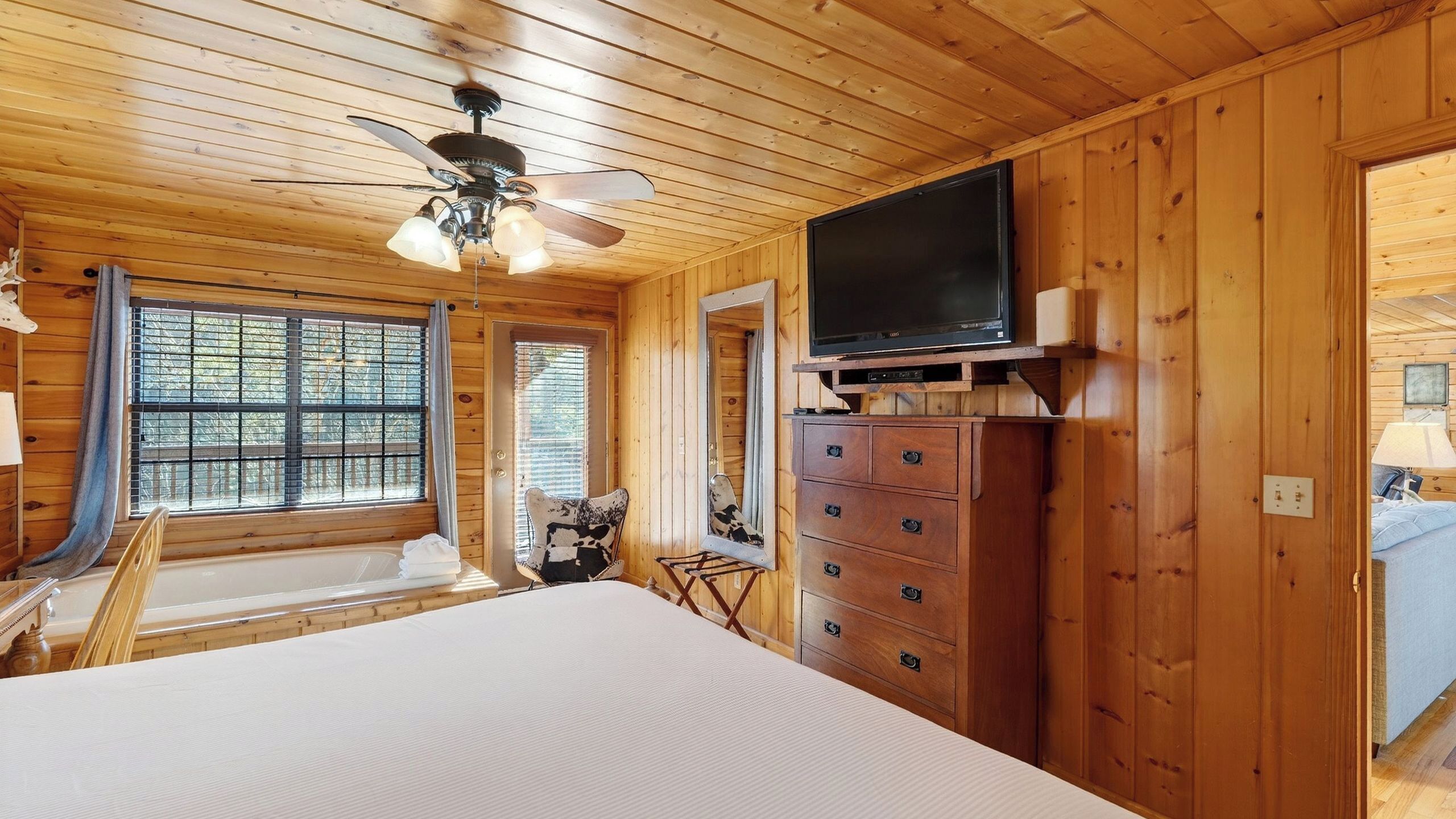 Une chambre dans une cabane en bois, avec un lit, une commode, une télévision et un ventilateur de plafond.