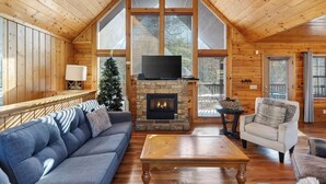 A cozy cabin interior with a stone fireplace, a television, a sofa, and a chair. - Grand Getaway Cabin by Avantstay A-frame Retreat + Hot Tub + Pool Access, Game Room Mins to Dollywood (Sevierville)
