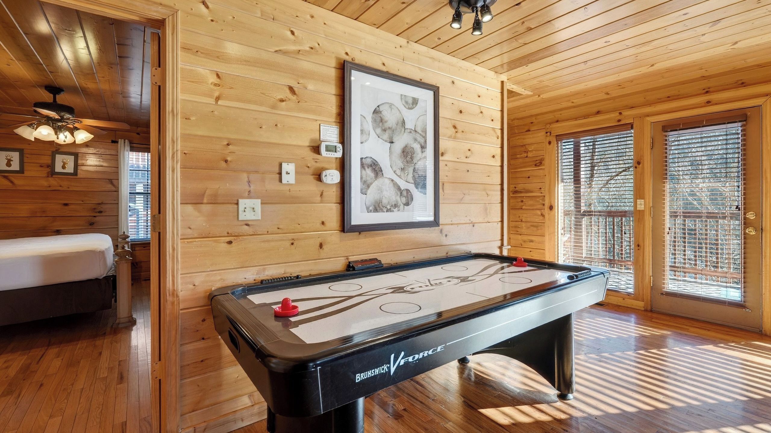 Una habitación con suelo de madera, una mesa de futbolín, un cuadro en la pared y una cama con cabecero.