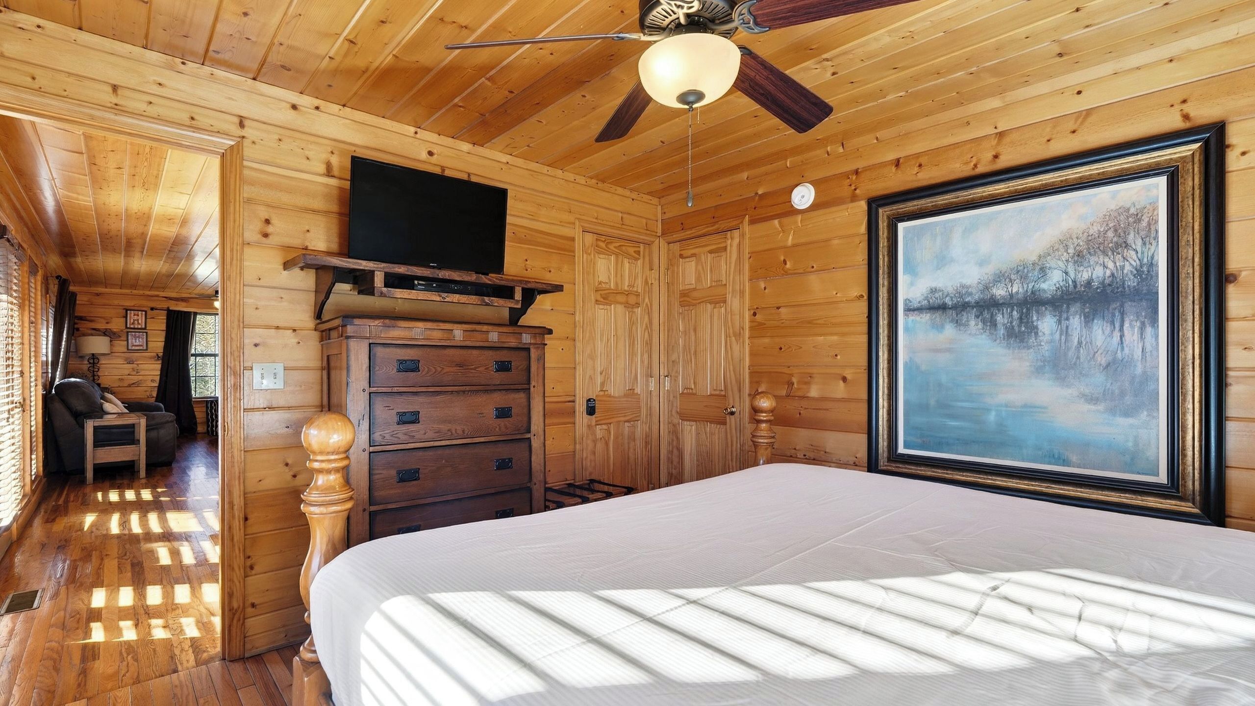 Ein Zimmer in einer Holzhütte mit einem Bett, einem Schminktisch und einem Gemälde eines Sees.