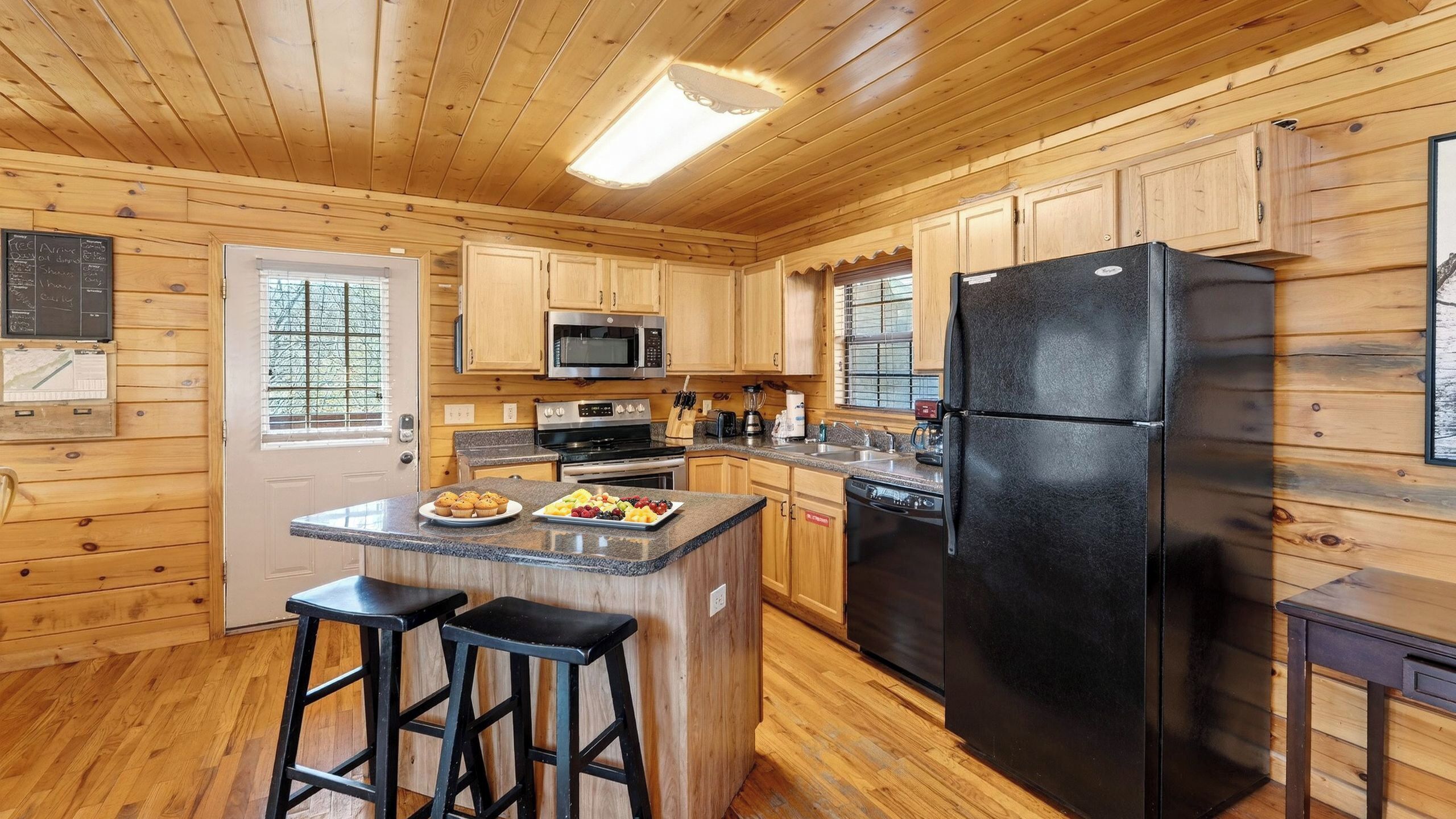 A wooden cabin kitchen with a central island, bar stools, a refrigerator, and a microwave.