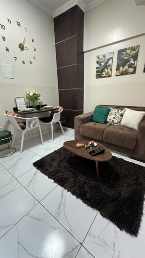 A living room with a brown sofa, a coffee table, a clock, and a dining area with chairs and a table. - Historic Manaus • 2 SZ • Walking to the Teatro Amazonas (Manaus)