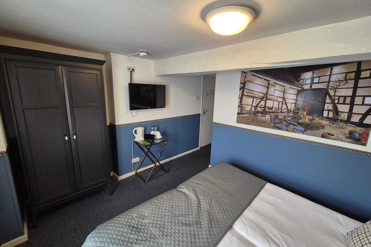Habitación de hotel con cama, escritorio con silla, televisor y un mural grande en la pared.