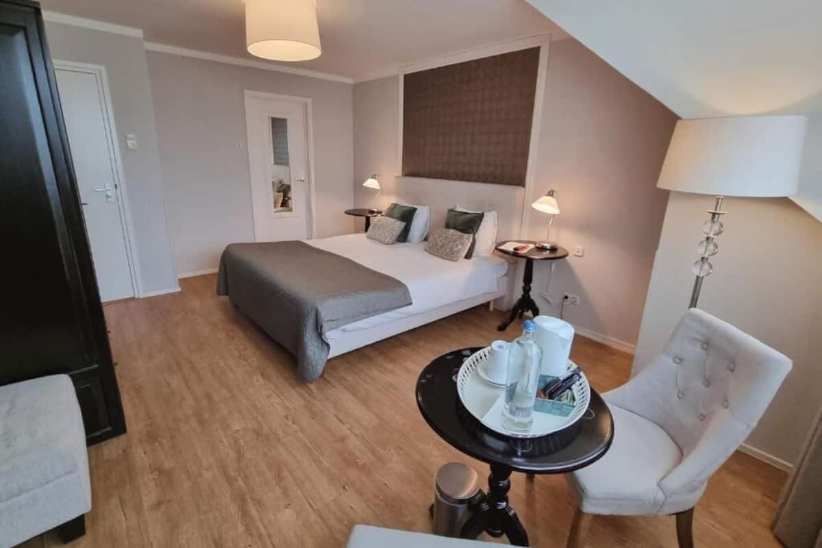 Una habitación de hotel con cama, mesitas de noche, una silla, una mesita con bandeja y una lámpara.