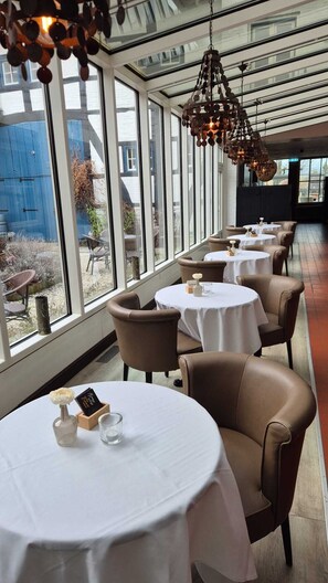 A restaurant with round tables, brown leather chairs, and a view through large windows. - Hotel Brull by Beautique Hotels (Mechelen)