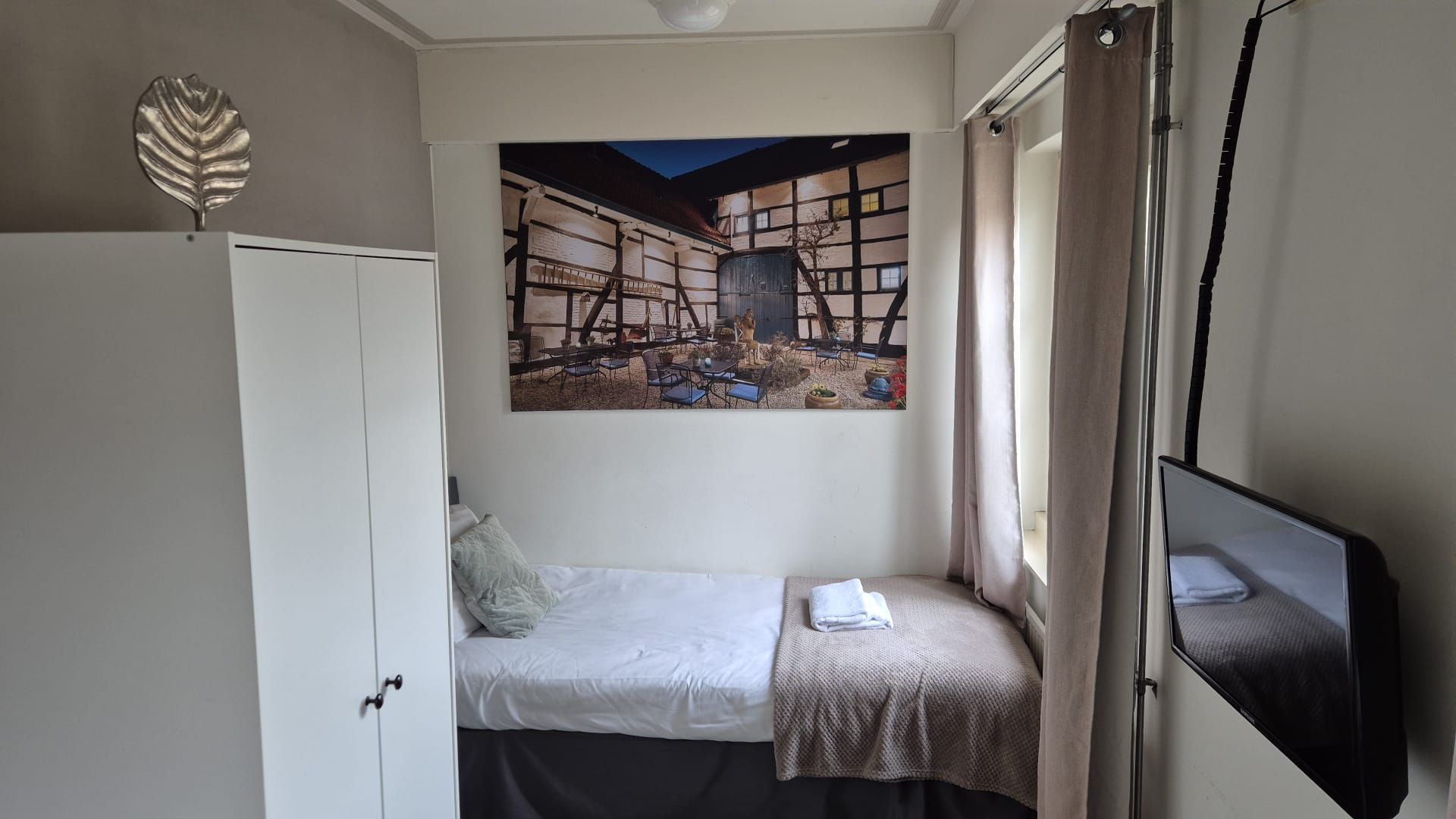 Une petite chambre à coucher comprenant un lit, une armoire, un tableau représentant un paysage et un téléviseur.