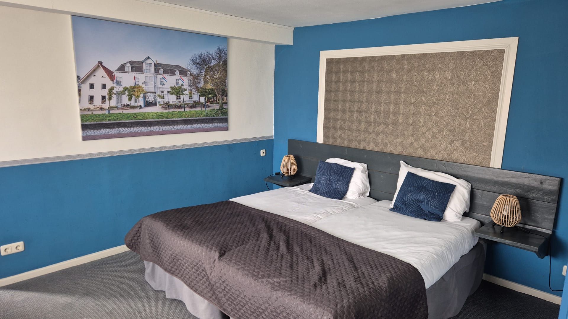 A bedroom with a large bed, two bedside tables, a wall-mounted artwork, and a window with a view of a building.