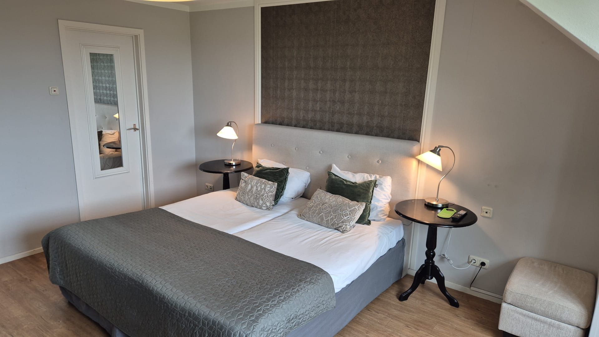 Een keurig opgemaakte slaapkamer met een bed, nachtkastjes en een stoel.