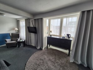 Habitación de hotel con cama, una silla, un escritorio, televisor y ventana con cortinas.