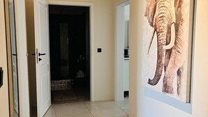 Un passadís amb un gran quadre d'elefant a la paret, una porta que dona a una habitació fosca i un paviment de rajoles.