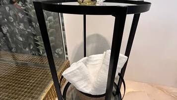 A round, black metal table with a glass top, a white tissue holder, and a small bottle of reed diffuser.