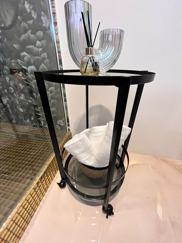 A round, black metal table with a glass top, a white tissue holder, and a small bottle of reed diffuser.