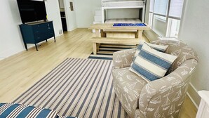 A modern living room with a sofa, a patterned armchair, a TV, a bunk bed, and a ceiling fan. - New Listing: perfect location, Sunshine Cottage,  a cute little gem in Lakeside! (Muskegon)