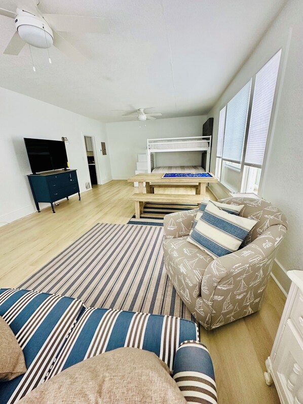 A modern living room with a sofa, a patterned armchair, a TV, a bunk bed, and a ceiling fan. - New Listing: perfect location, Sunshine Cottage,  a cute little gem in Lakeside! (Muskegon)