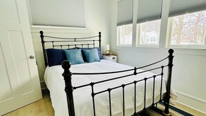 A bedroom with a metal bed frame, white bedding, a striped rug, and a window with blinds. - New Listing: perfect location, Sunshine Cottage,  a cute little gem in Lakeside! (Muskegon)