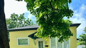 A yellow house with a front porch, a tree, and a clear sky. - New Listing: perfect location, Sunshine Cottage,  a cute little gem in Lakeside! (Muskegon)