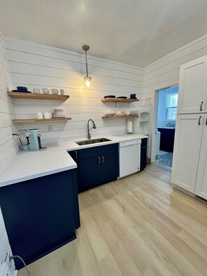 A modern kitchen with white cabinetry, wooden shelves, and a built-in dishwasher. - New Listing: perfect location, Sunshine Cottage,  a cute little gem in Lakeside! (Muskegon)