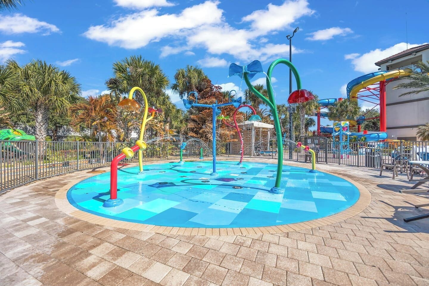 Parque acuático con piscina central, toboganes acuáticos de colores y palmeras al fondo.