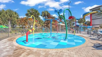 Parque acuático con piscina central, toboganes acuáticos de colores y palmeras al fondo.