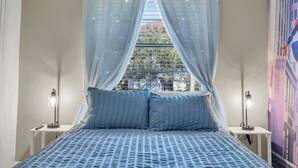 A bedroom with a bed, two bedside tables, a window with sheer curtains, and a wall-mounted lamp. - Amazing Spider | Disney, Slides & River (Kissimmee)