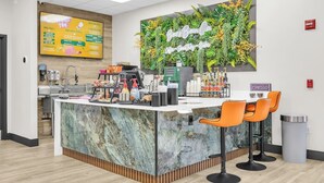 Een koffietent met een marmeren toonbank, oranje stoelen, een menubord en een hangplant aan de muur.