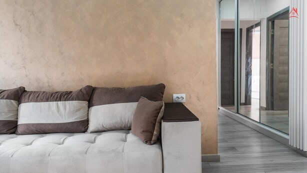 A modern living room with a sofa set against a textured wall, a small table with a power outlet, and a view through a glass door to an outdoor area. - Cozy 2-bedroom apartment in beautiful București with AC (București)